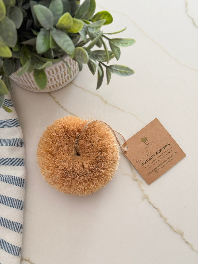 Coconut scrubber with a label on a marble surface next to a plant and striped towel.