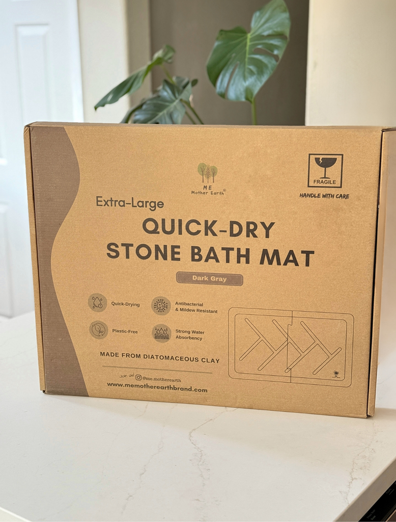 Cardboard box of an extra-large quick-dry stone bath mat on a light surface with a plant in the background.